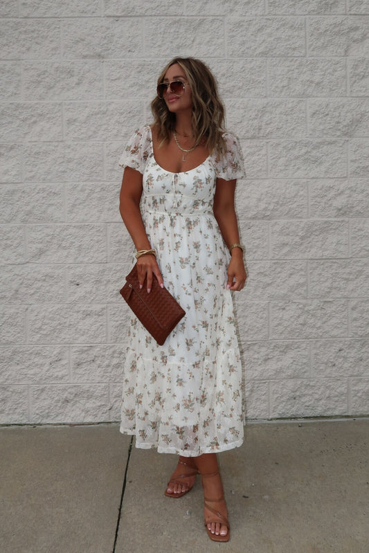 Woman wearing the Lauri Cream Floral Print Sweetheart Midi Dress with brown sandals, sunglasses, and a brown clutch.