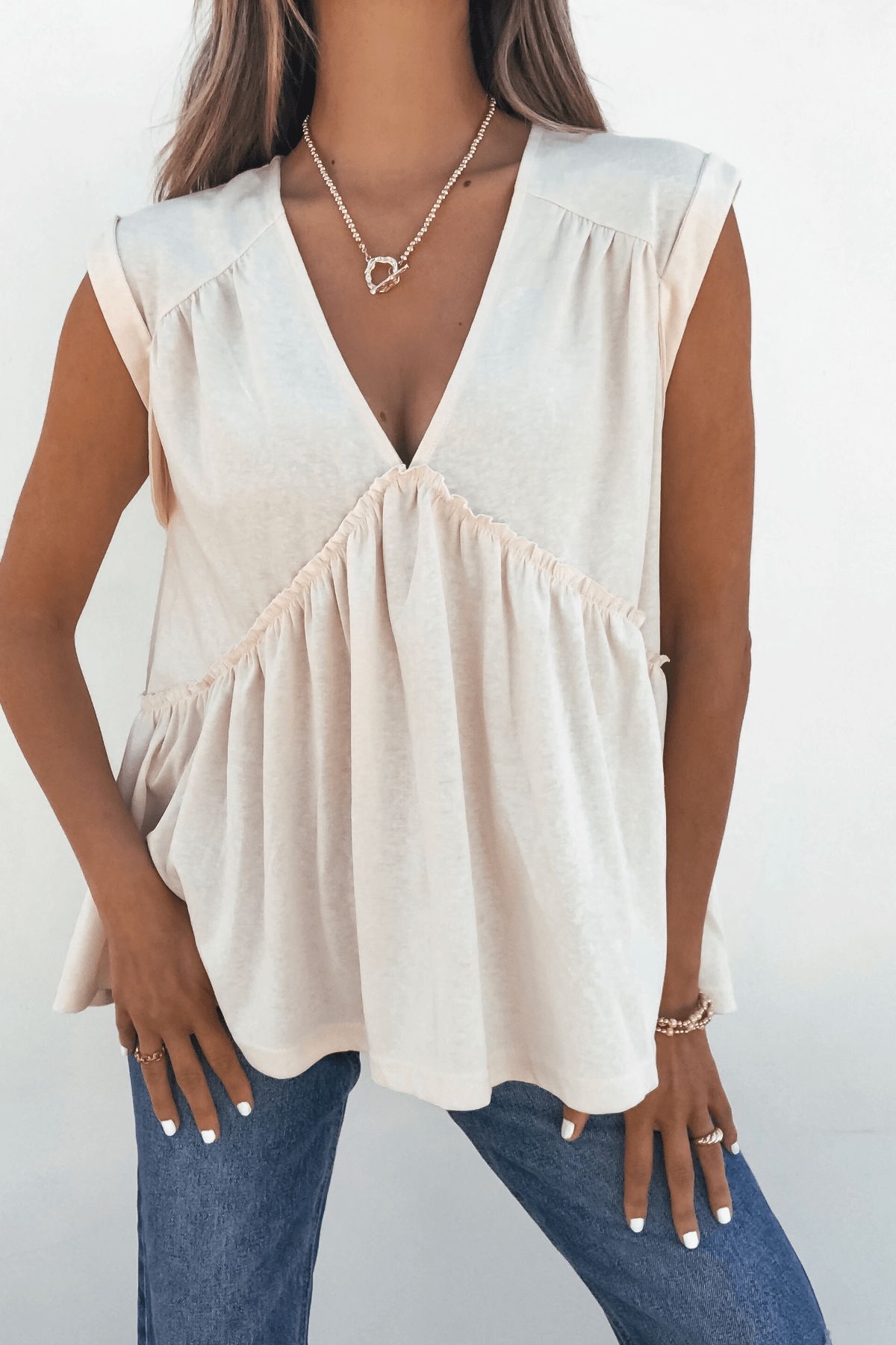 Woman wearing Lena's Carefree Afternoon Cream Babydoll Top—DOORBUSTER—styled boho-chic with jeans and gold jewelry.