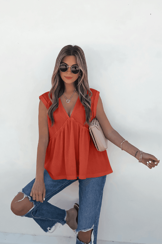 Woman wears Lena's Carefree Afternoon Coral Babydoll Top with ripped blue jeans, sunglasses, and a beige purse against a white background.