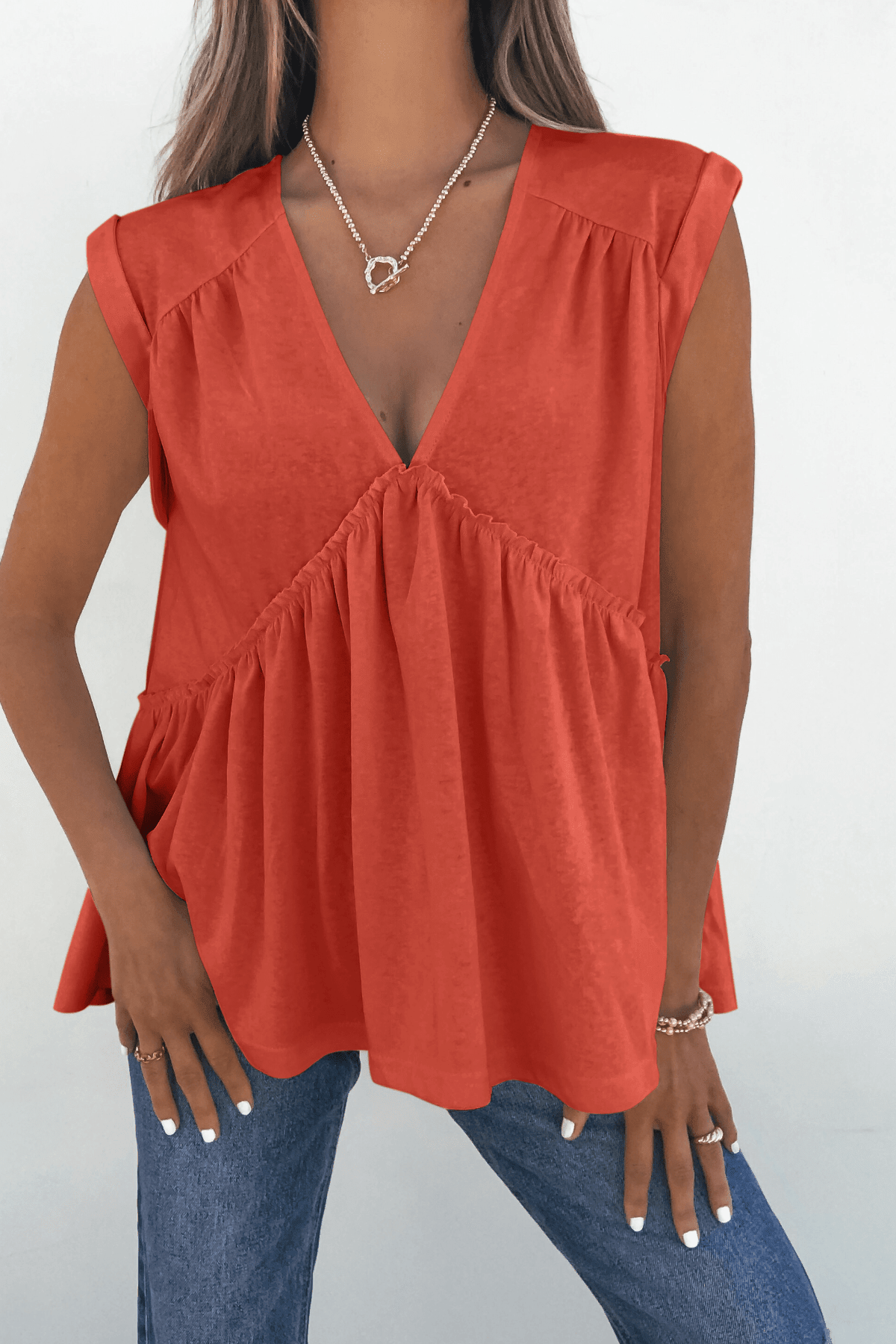 Woman in Lena's Carefree Afternoon Coral Babydoll Top and blue jeans, styled with rings and a necklace.