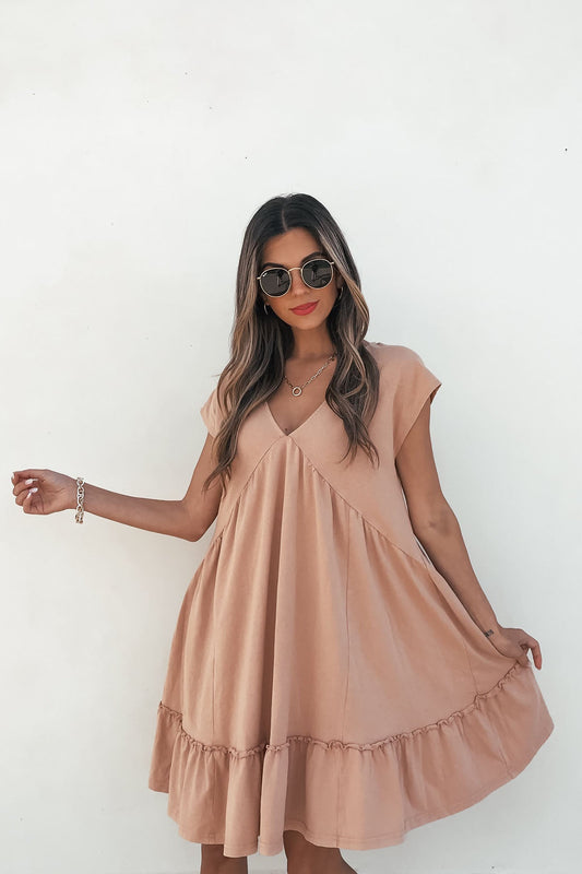 A woman models the Light Apricot V Neck Mini Dress, holding the hem against a white background.