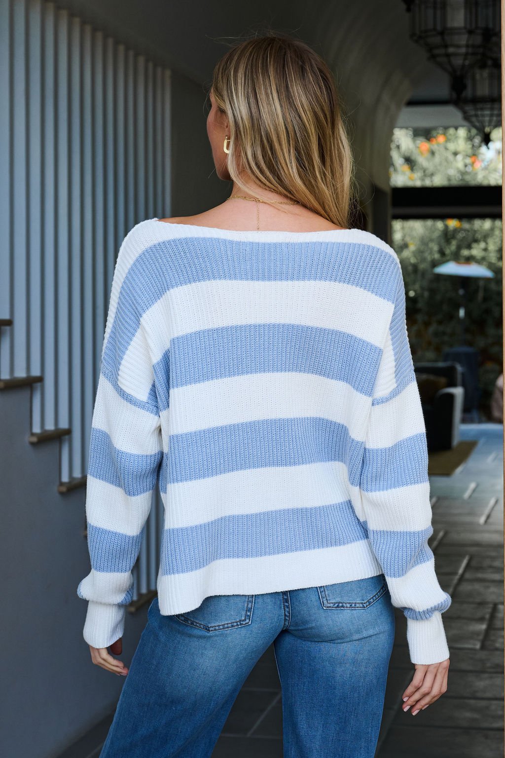 Woman with long blonde hair wears the Callahan Light Blue and White Striped Sweater and blue jeans, seen from behind indoors.