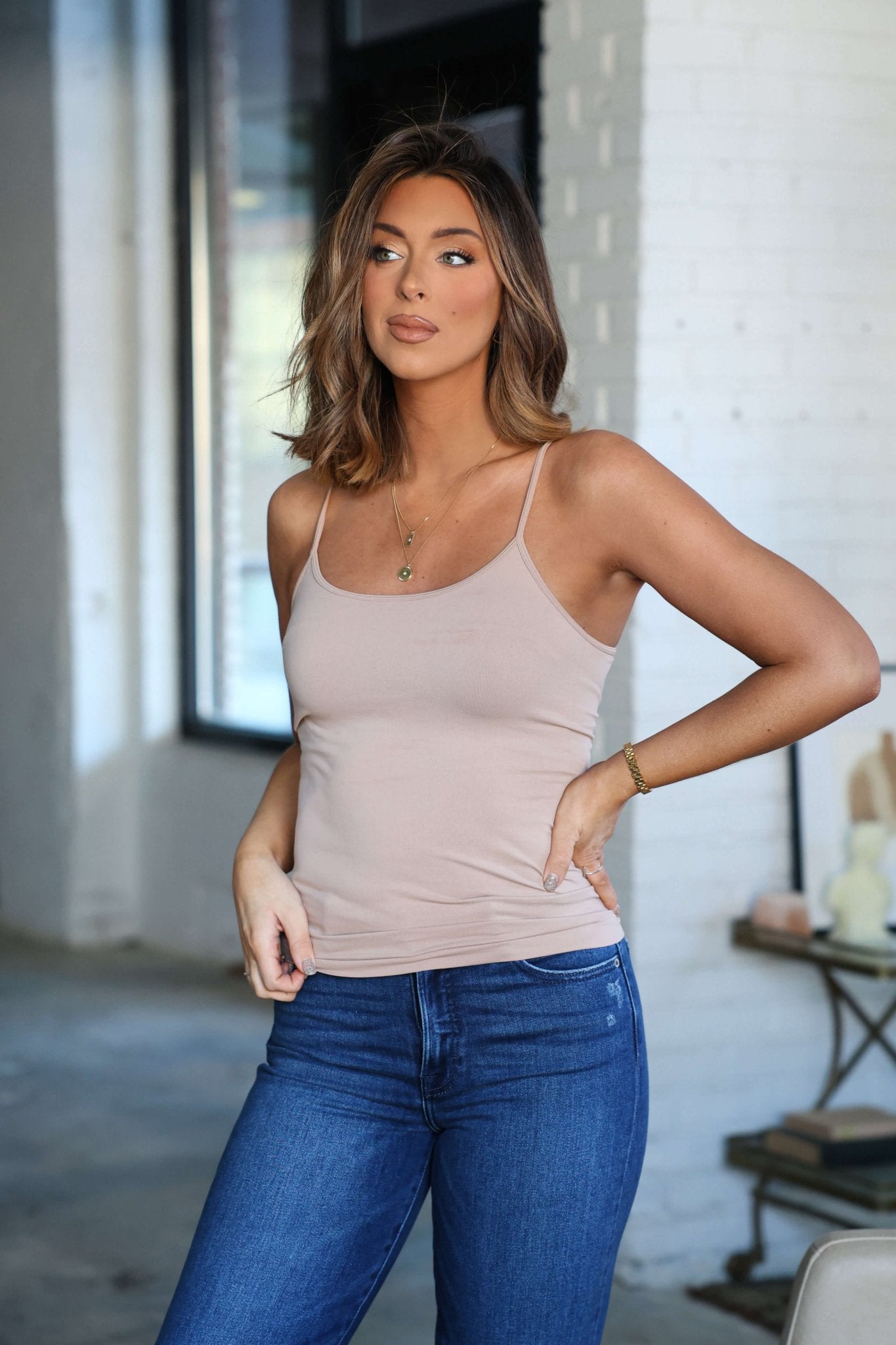 Woman with shoulder-length brown hair wears a Light Taupe Seamless Cami Tank Top with adjustable straps and blue jeans, indoors.