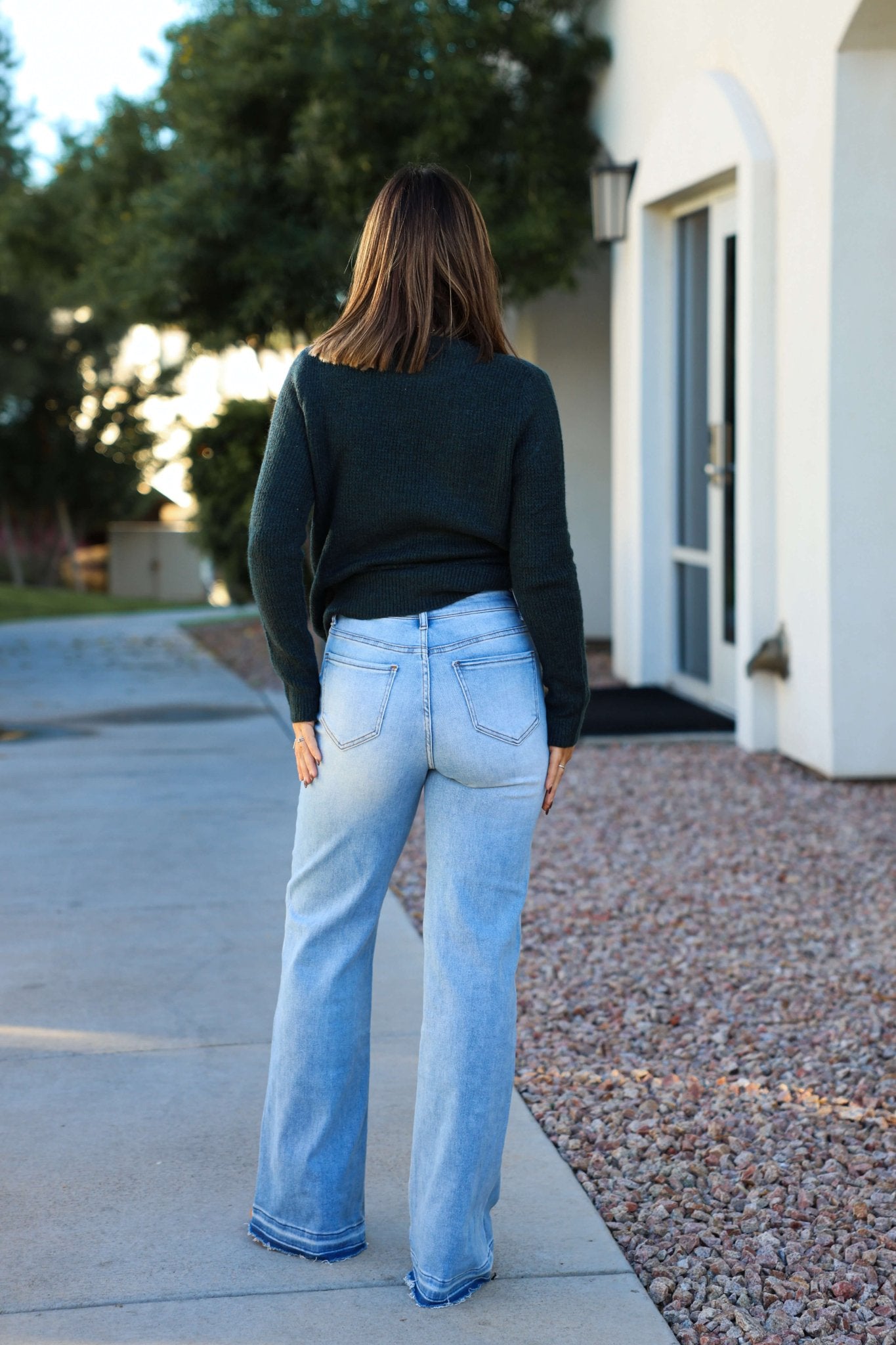 A woman stands outdoors with her back to the camera, wearing Light Wash Seam Detail Wide Leg Jeans near a building and trees.
