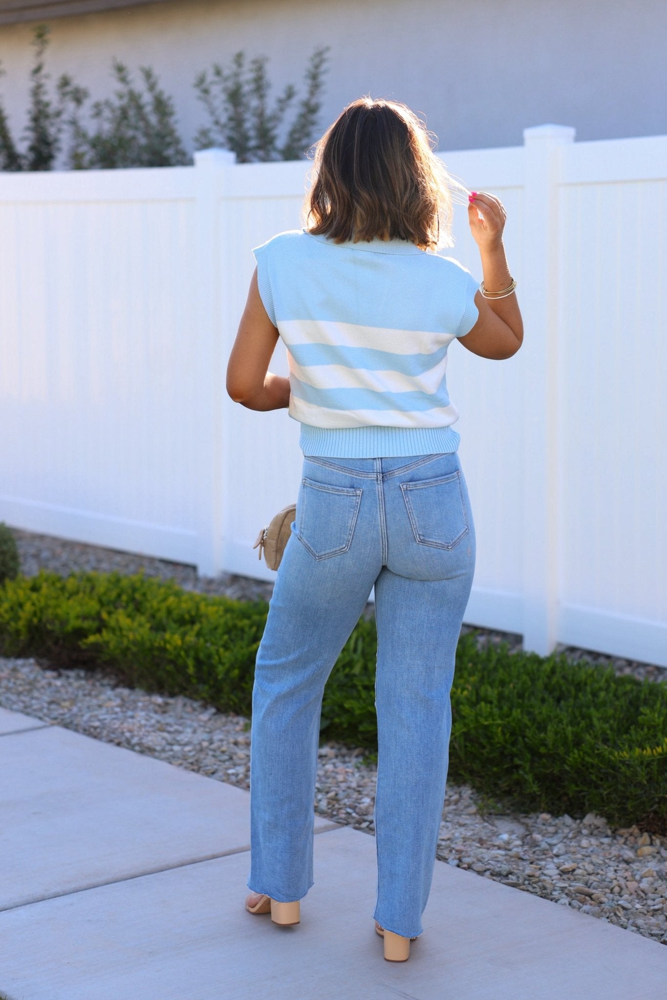 A woman in Light Wash Super High Rise Dad Jeans stands on a sidewalk near a white fence and green bushes.