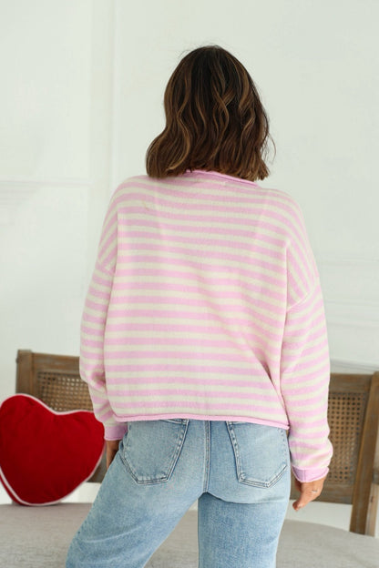 A person with wavy brown hair wears the Lilac Pink Striped Button Down Sweater and light blue jeans, shown from the back.