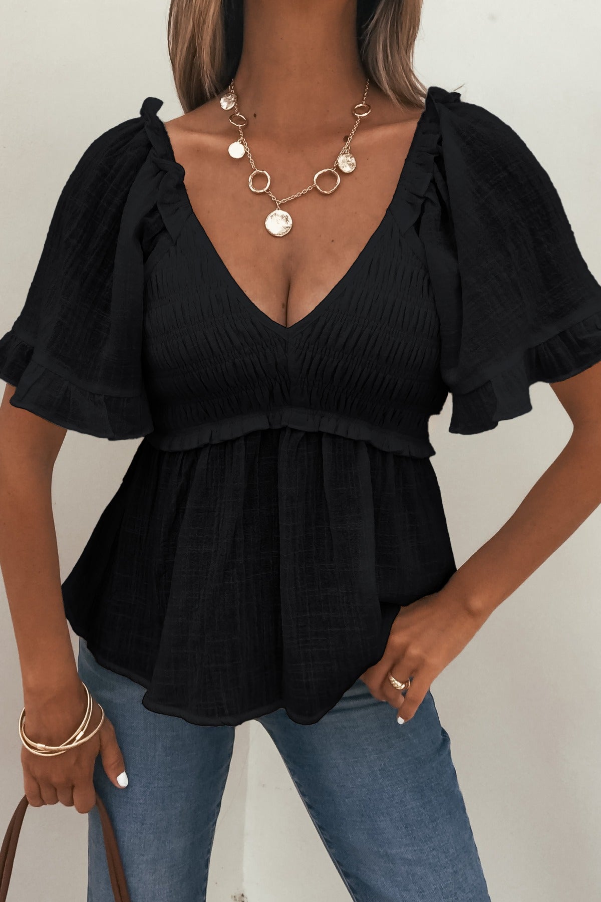 Woman in Lola Black Ruffled Babydoll Top, blue jeans, gold jewelry, and brown handbag.
