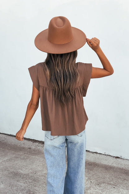 Woman with long hair in a wide-brimmed brown hat, Lola Button Up Lace Top - Mocha, and light blue jeans stands with back to camera.