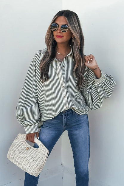 Woman in sunglasses and red lipstick wears the Loose Ends Striped Shirt - Olive, blue jeans, and a woven handbag against a white background.