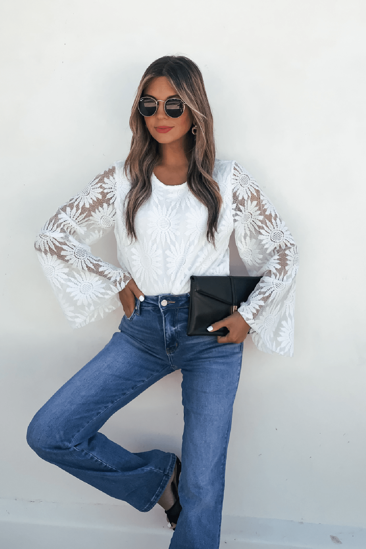 Woman wears the Louisa White Floral Lace Bodysuit with blue jeans, sunglasses, and a black clutch against a white wall.
