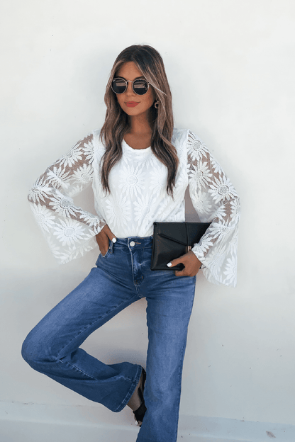 Woman wears the Louisa White Floral Lace Bodysuit with blue jeans, sunglasses, and a black clutch against a white wall.
