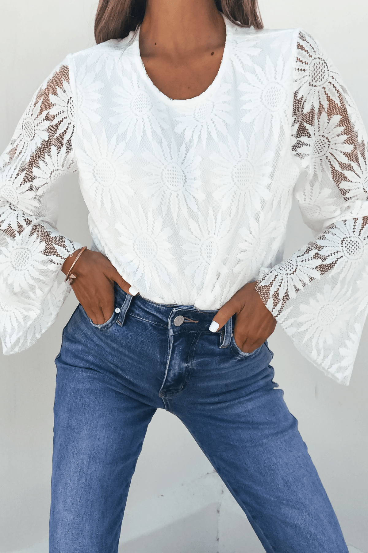 The Louisa White Floral Lace Bodysuit is styled with flared sleeves and blue jeans for a chic, romantic look.