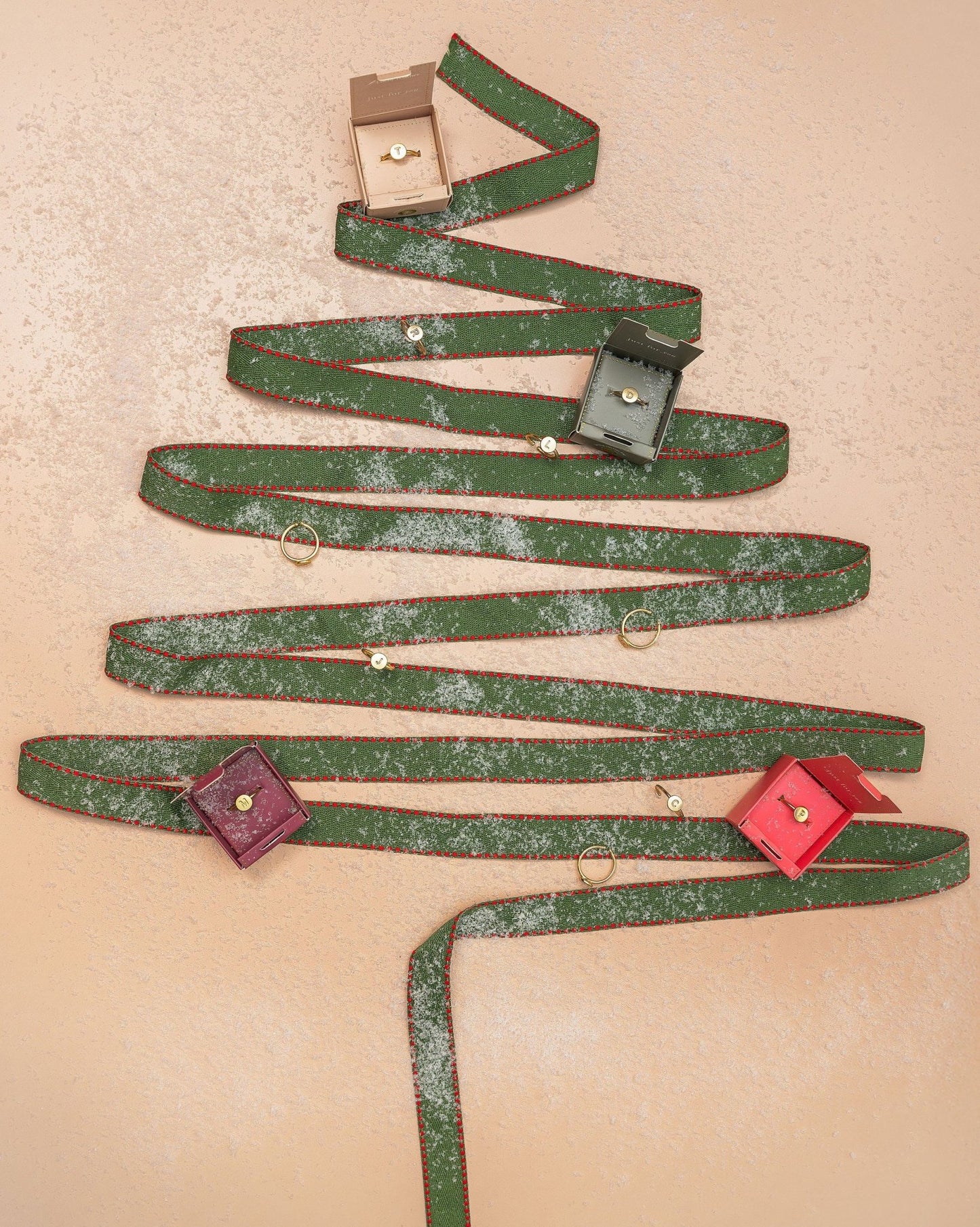 A Lucky Feather Gold Initial Pendant Ring on a peach background with gift boxes and faux snow.