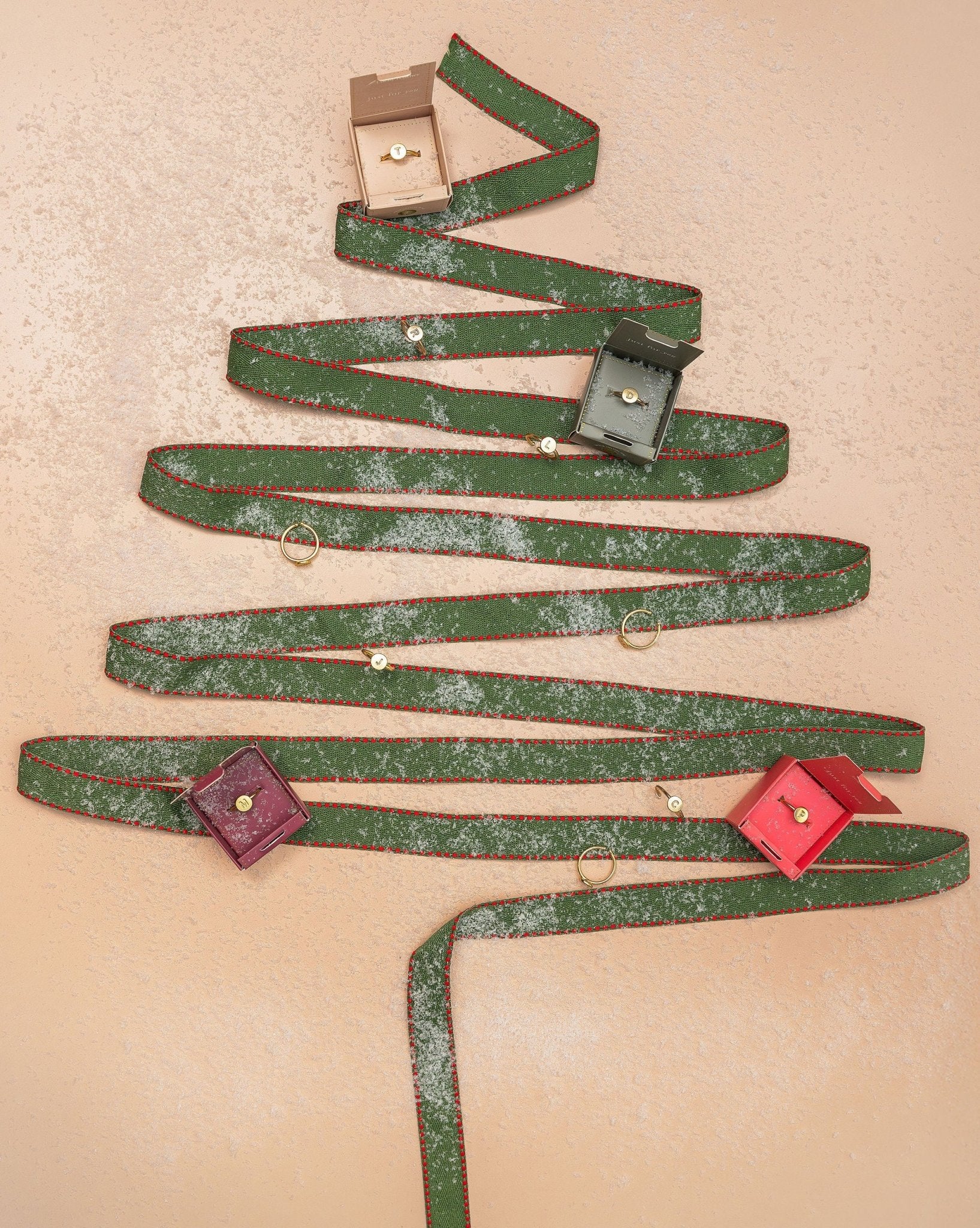 A Lucky Feather Gold Initial Pendant Ring on a peach background with gift boxes and faux snow.