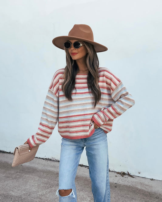 A person wearing a Multi Stripe Long Sleeve Sweater - Pink, distressed jeans, a wide-brim hat, and sunglasses, holding a small clutch.