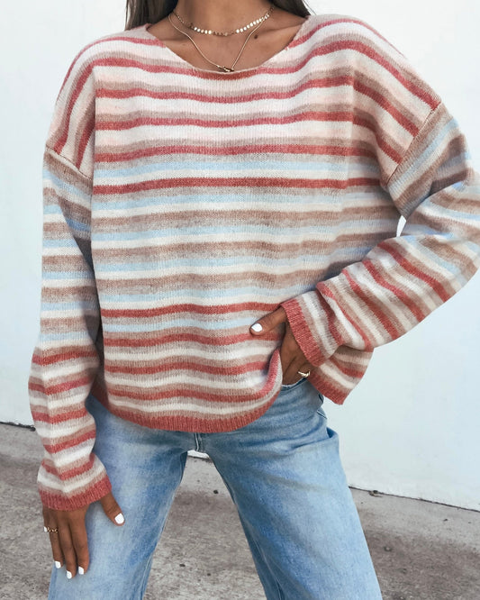A person wearing a Multi Stripe Long Sleeve Sweater - Pink with oversized sleeves paired with light-wash blue jeans.
