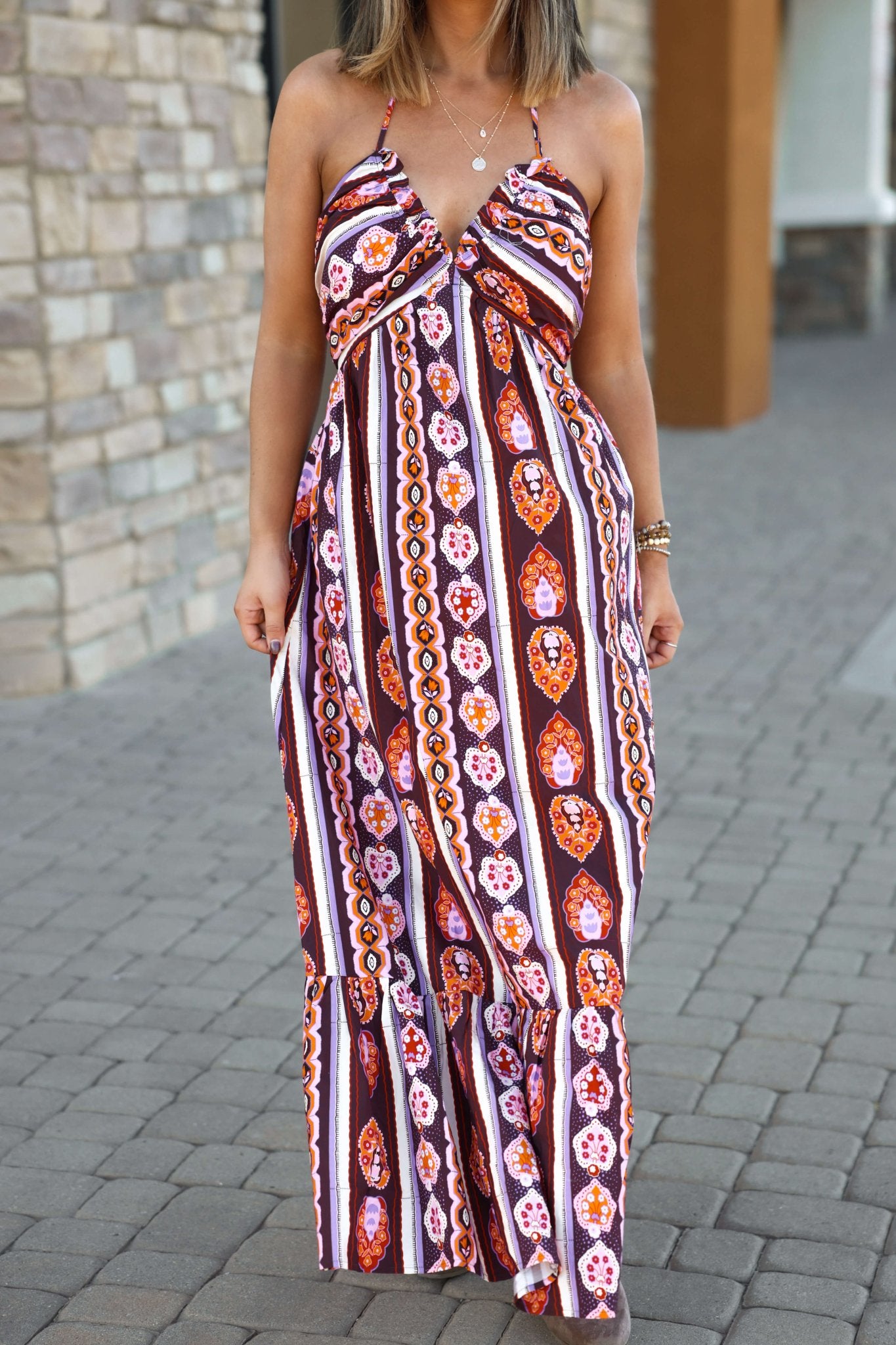 Woman in the Maple Moments Halter Maxi Dress - Multi - DOORBUSTER, with a deep halter V-neck, on a cobblestone walkway.