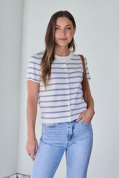 Woman in the Marina Blue and White Striped Sweater Cardigan, light blue jeans, and a brown bag stands indoors.
