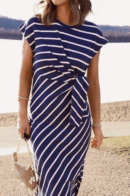 Woman in the Marina Mornings Navy Striped Midi Tie Dress—an ideal summer look near water, paired with a woven handbag.