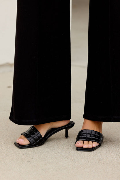 Someone stands on a light surface in black wide-leg pants and Matisse Rosanna Kitten Heels.