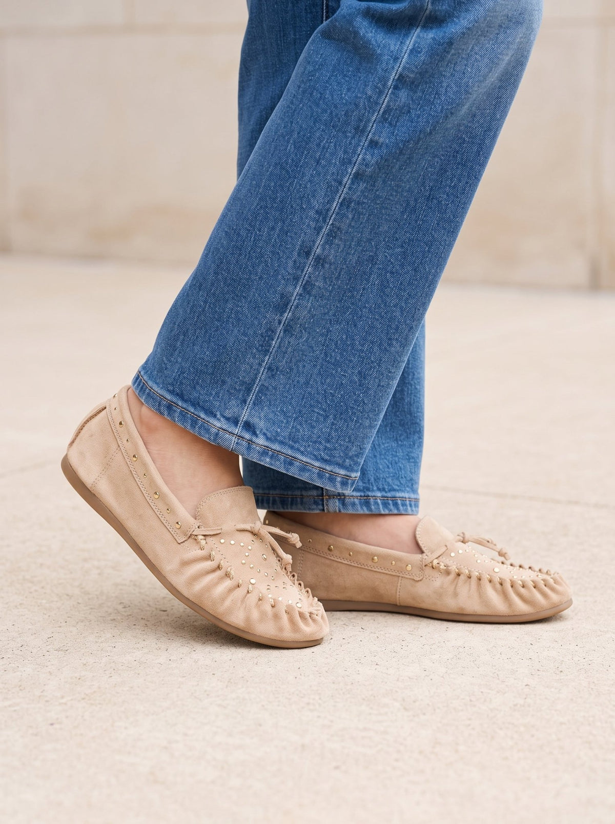 A person wears blue jeans and MATISSE SEBASTIAN NATURAL SLIP ON MOCCASINS, which are light tan with metallic stud details.