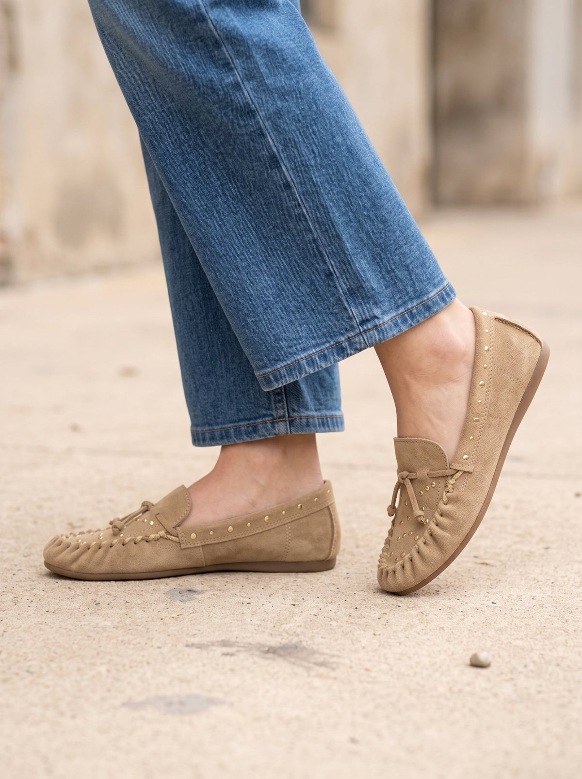A person wearing tan MATISSE SEBASTIAN NATURAL SLIP ON MOCCASINS with tassel details, side stitching, and small metallic studs.