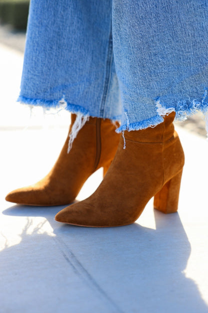 A person in frayed hem blue jeans and Matisse Spencer Camel Heeled Ankle Booties stands on a sunny sidewalk.