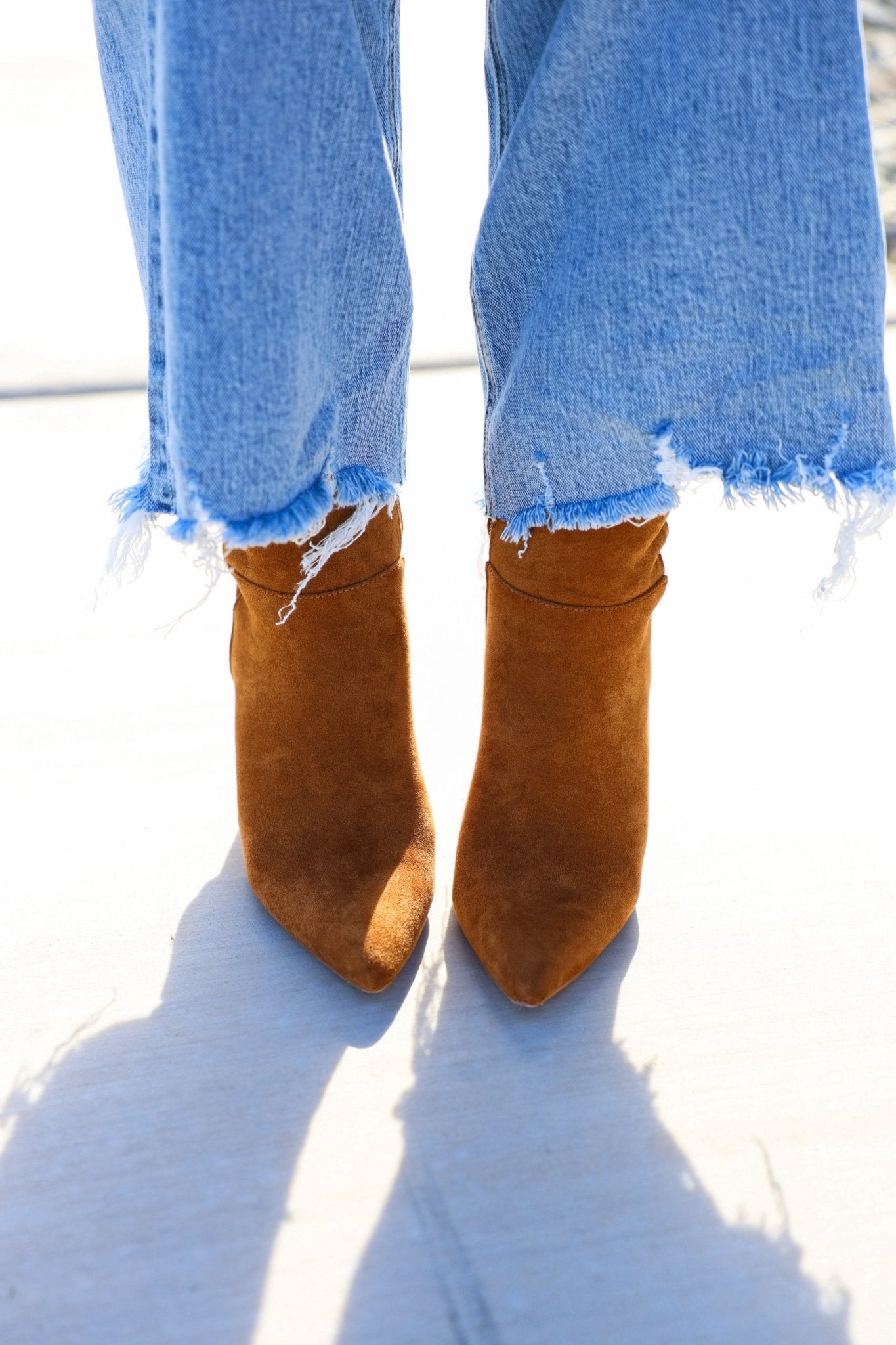Person wearing frayed hem blue jeans and Matisse Spencer Camel Heeled Ankle Booties, standing on a light surface.