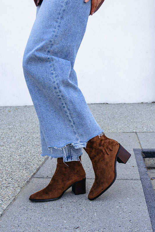 Person in light blue frayed jeans and brown Matisse Warren Heeled Ankle Booties, standing on a sidewalk.