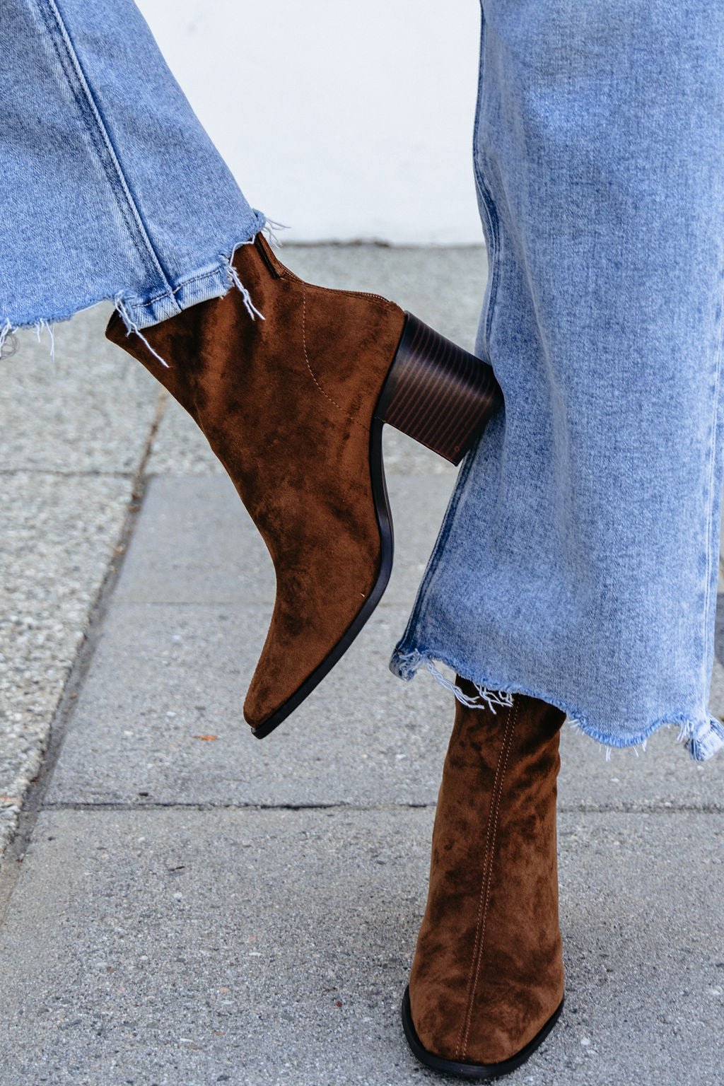 Person in frayed blue jeans and Matisse Warren Heeled Ankle Booties in brown, standing on a sidewalk.