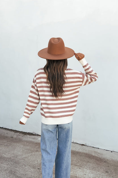 A person in jeans and a Mauve Striped Waffle Knit Sweater stands facing a white wall, seen from behind.