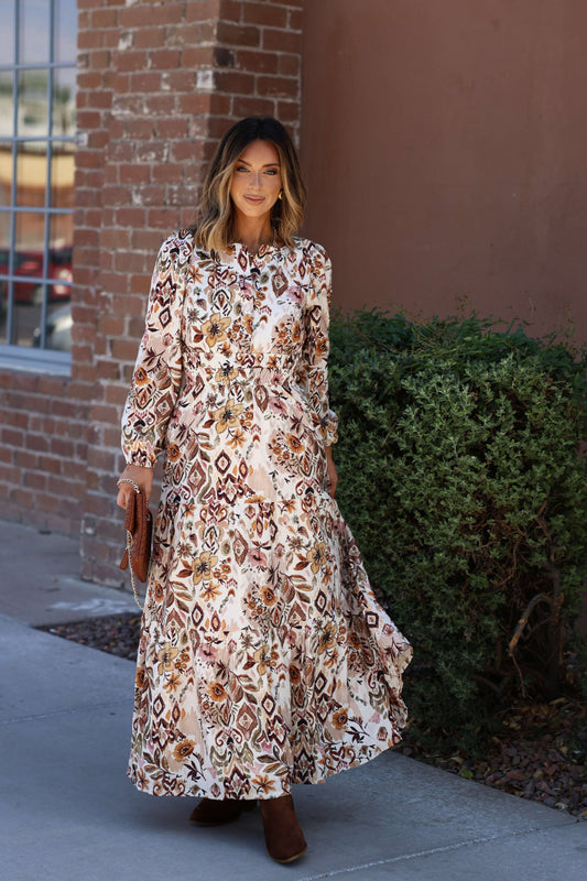 Woman stands on a sidewalk near a brick wall in the Meadow Brown Print Tiered Maxi Dress - FINAL SALE.