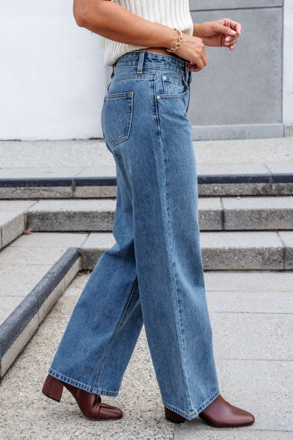 Person wearing Medium Wash Baggy Wide Leg Jeans, a white knit top, and brown ankle boots, walking on stone steps.