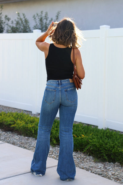 A woman wears Medium Wash Flare Denim Jeans and a black tank top outside, sunlight highlighting her hair.