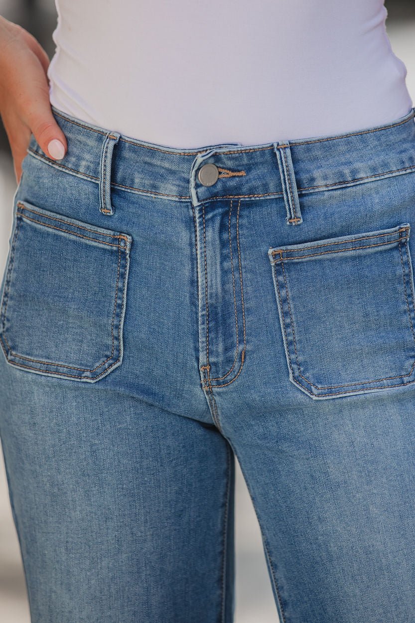 Close-up of a person wearing Medium Wash Patch Pocket Wide Leg Jeans and a white top, hand near the front pocket.