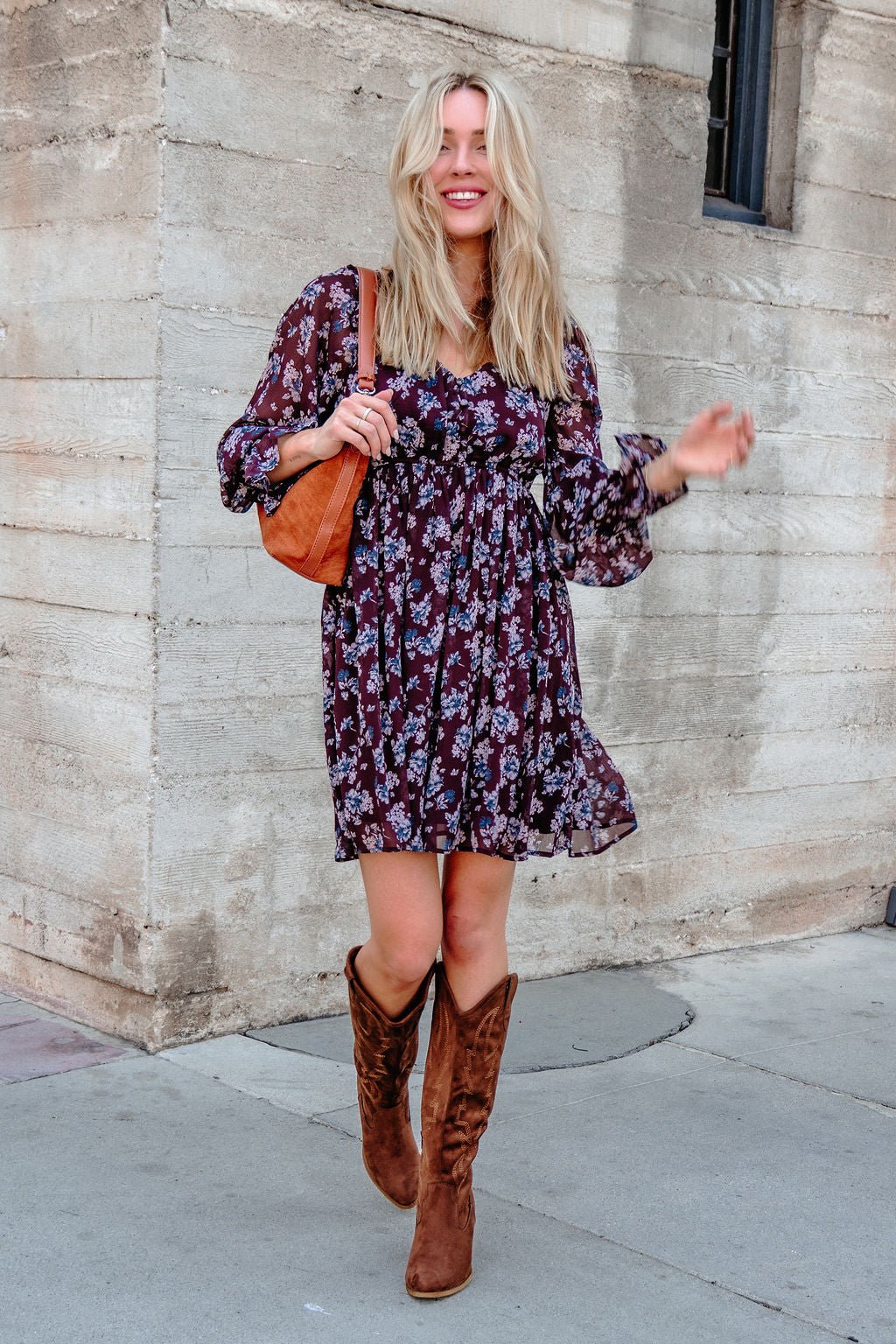 A woman in the Merlot Floral Chiffon Babydoll Mini Dress smiles as she walks down the sidewalk.