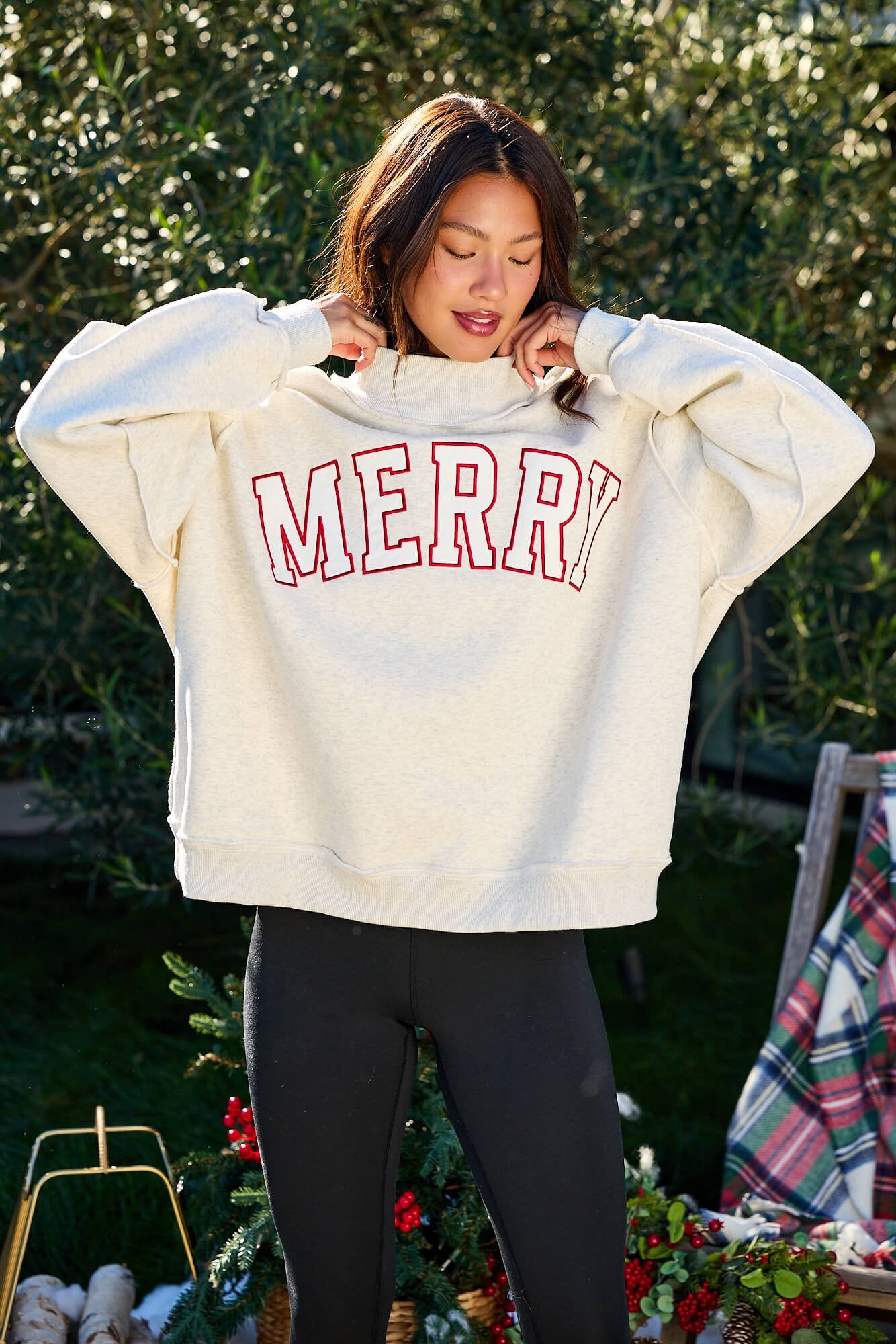 Woman outdoors in a Merry Grey Oversized Sweatshirt - FINAL SALE and black leggings, with festive holiday decor nearby.