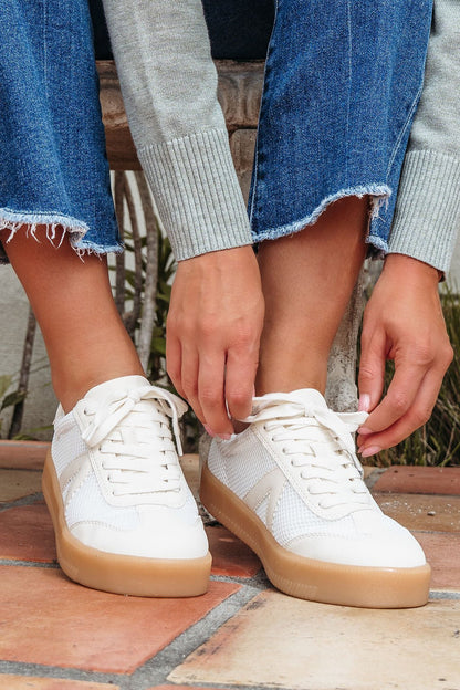 Sitting on a bench, a person in frayed hem jeans ties the laces of Mia Axel Natural Lace Up Sneakers - FINAL SALE.