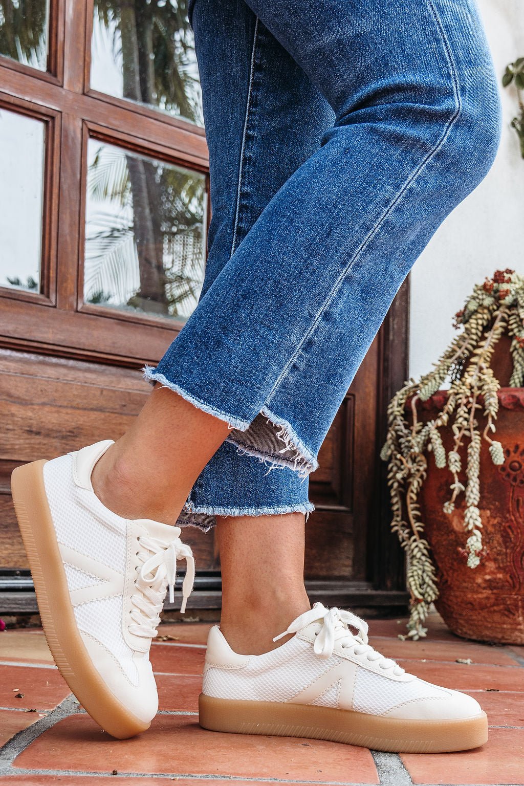 Someone in frayed hem blue jeans and Mia Axel Natural Lace Up Sneakers stands on terracotta tiles by a clay potted plant.