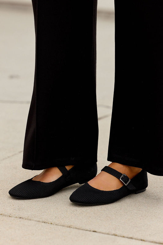 Someone wearing MIA Brita Ballet Flats - Black and black pants stands on light-colored pavement.
