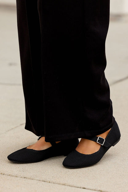 Model wears MIA Brita Ballet Flats - Black with a Mary Jane strap and round toe, styled with black wide-leg pants on a light surface.