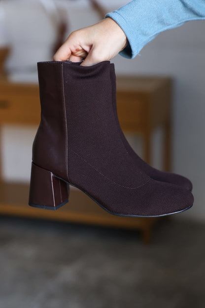 A hand holds up MIA Bronwen Brown Heeled Ankle Booties with block heels and a textured fabric finish.