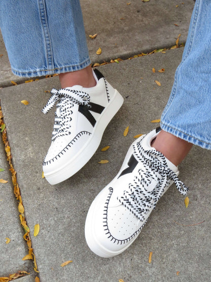 MIA Itzia Black and White Stitched Sneakers pair perfectly with blue jeans for comfy, casual style on a leaf-strewn sidewalk.