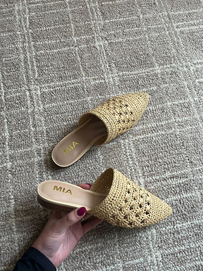 A hand holds a MIA Jany Natural Pointed Mule; the matching shoe rests on a tan patterned carpet.