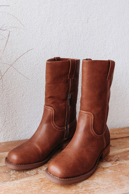 A pair of MIA Miley Mid Calf Boots in tan, featuring side zippers, on a wooden surface with a light textured wall background.
