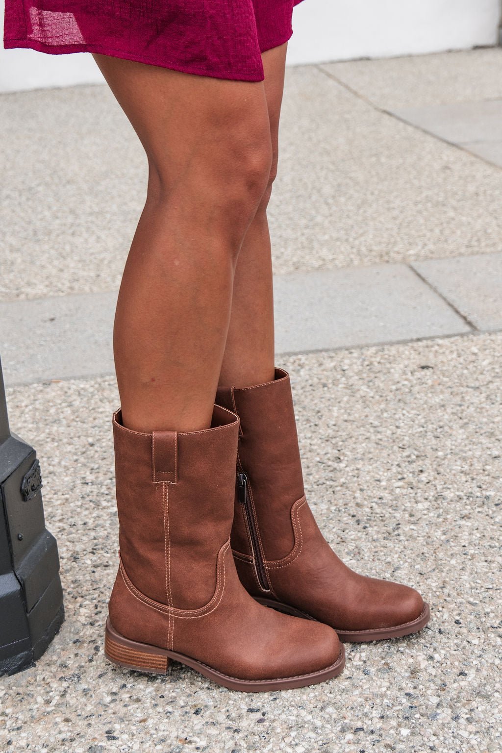 Someone in MIA Miley Mid Calf Boots - Tan and a burgundy skirt stands on a textured outdoor sidewalk.