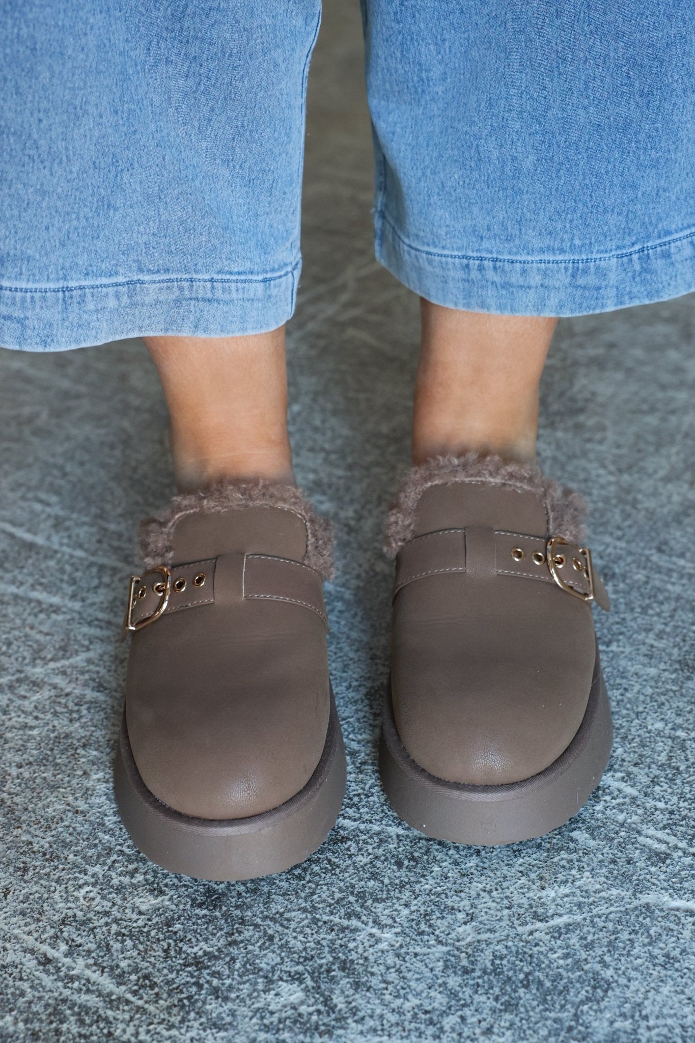 Person wears MIA Sugary Taupe Sherpa Mule loafers and cropped blue jeans, standing on a textured gray floor.