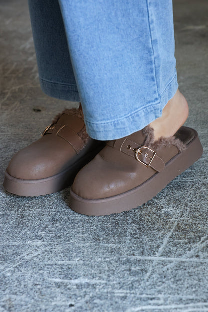 Wearing light blue jeans and MIA Sugary Taupe Sherpa Mule slip-ons, standing on a textured gray floor.