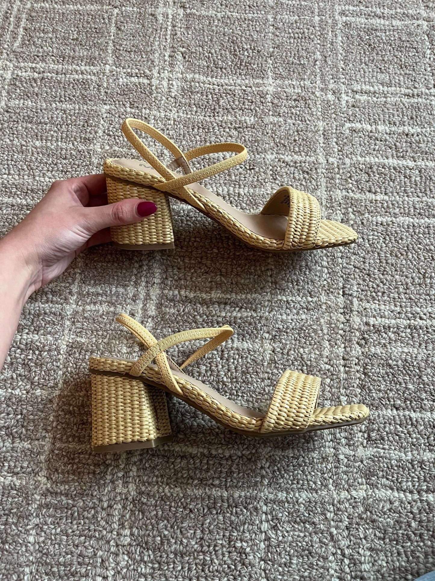 A hand holds the MIA Zissy Natural Strappy Heels, a pair of woven block heel sandals, on a textured carpet.
