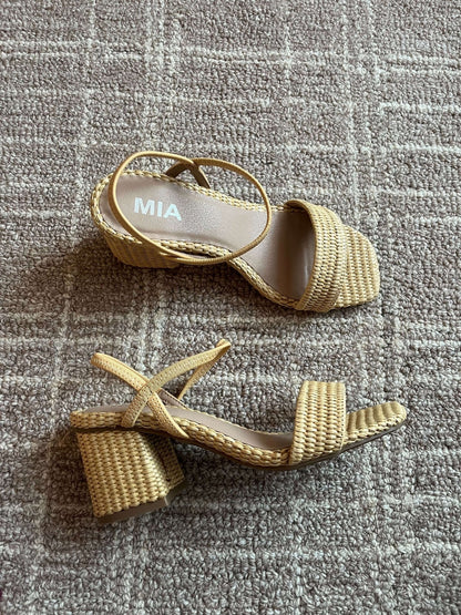 A pair of MIA Zissy Natural Strappy Heels with woven block heels rest on a textured beige carpet.